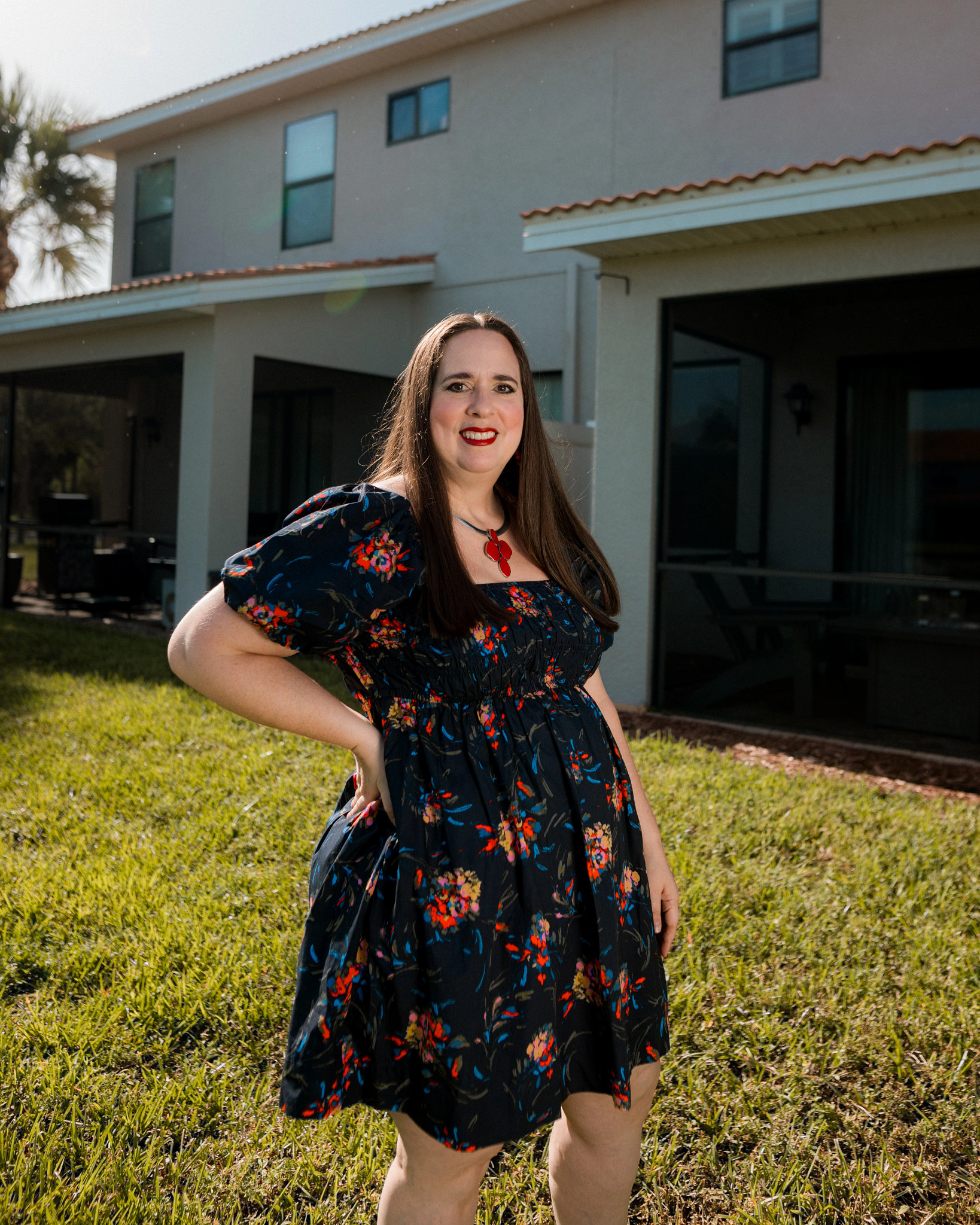 A person stands outdoors in front of a residential home wearing a patterned dress