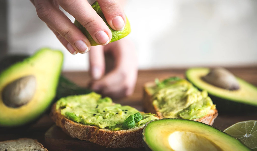 A close-up view of a person making a tomato and avocado sandwich