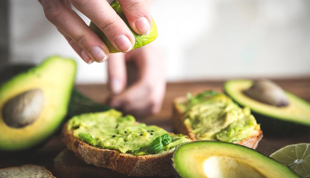 A close-up view of a person making a tomato and avocado sandwich