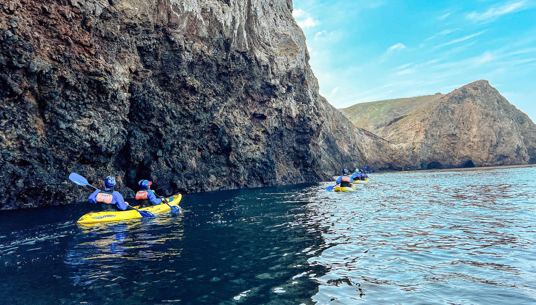 kayakers travel along cliffs and sea caves