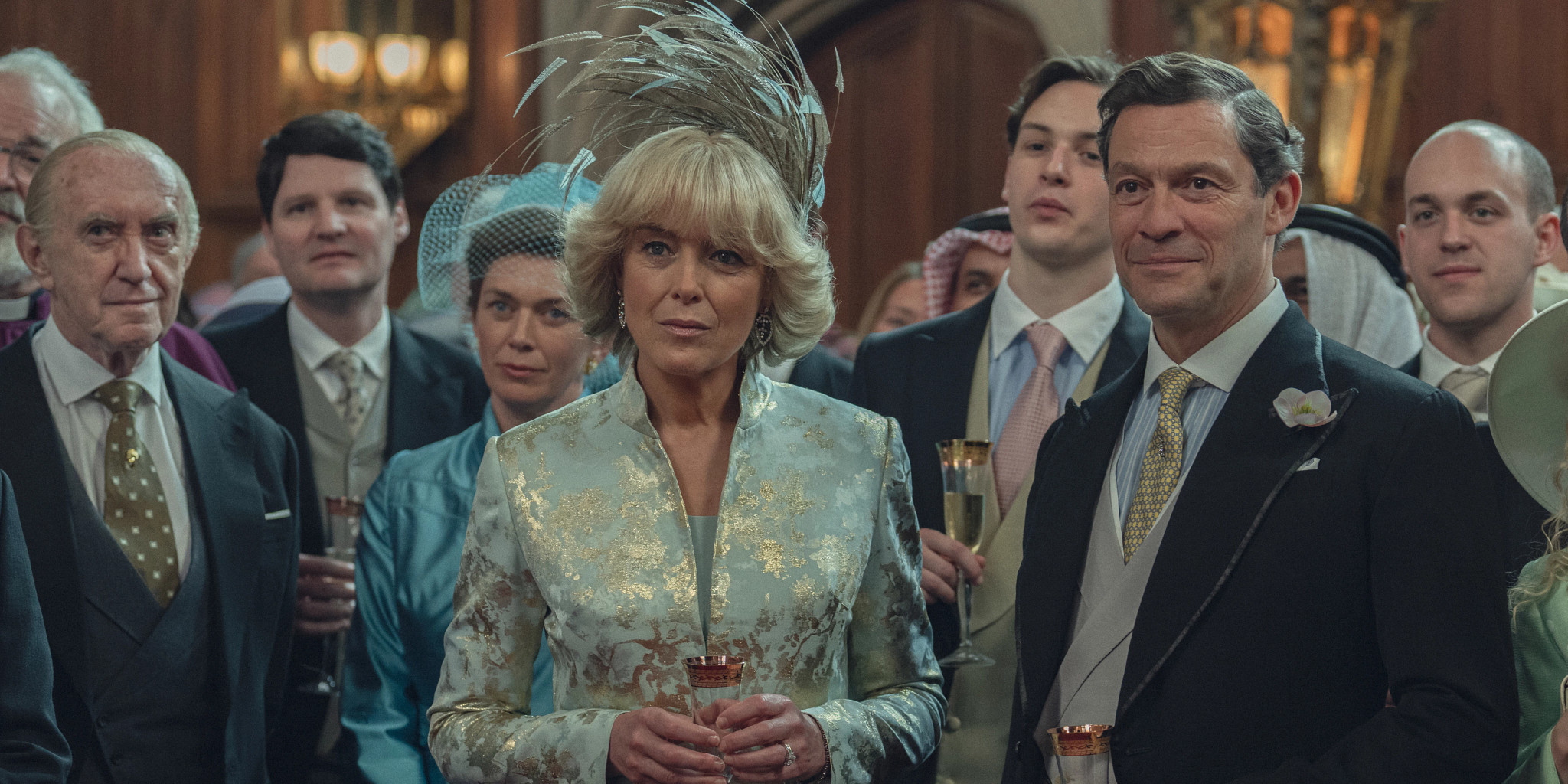 The Crown Olivia Williams and Dominic West standing next to each other with a group of people behind them in a scene from the Netflix series The Crown
