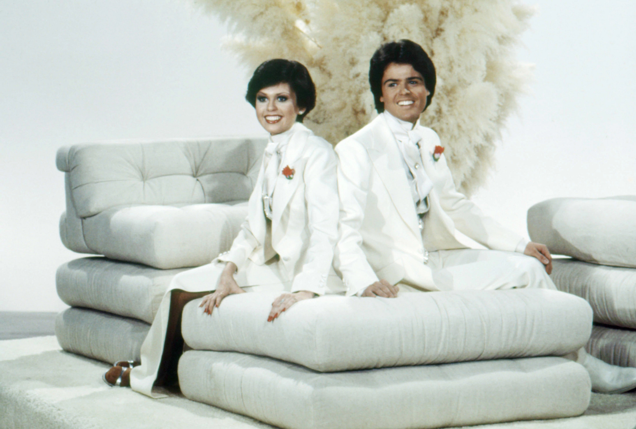 donny and marie osmond posing together in white suits with red boutonnieres