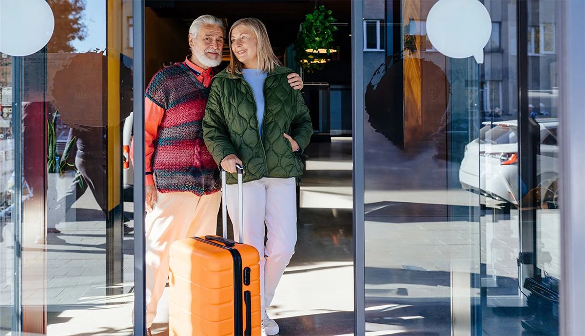 Mature couple walking out of the lobby of a luxury hotel rolling an orange suitcase