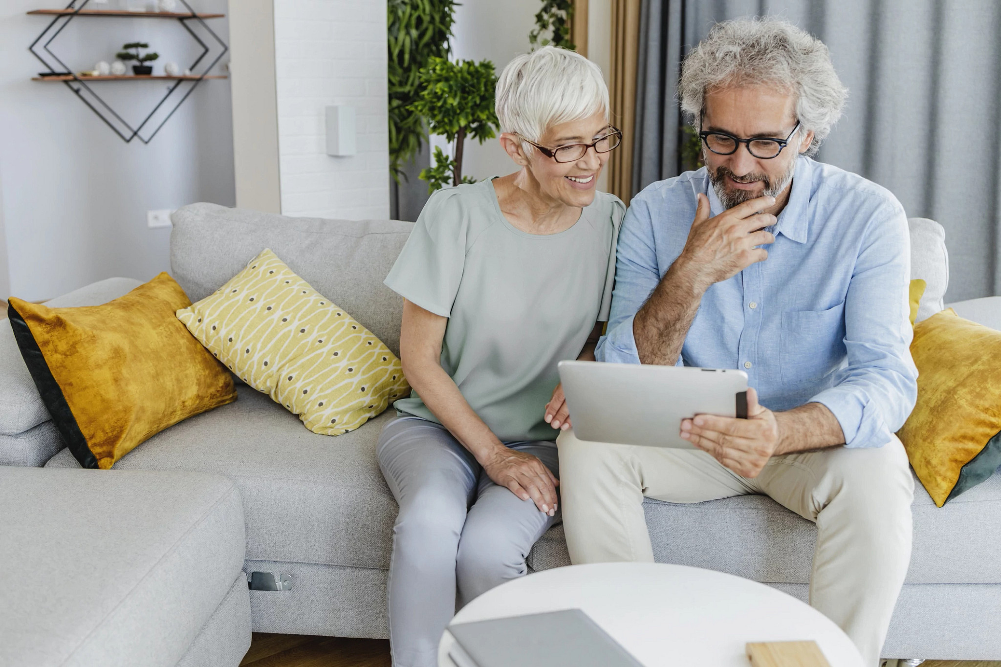 Senior men and woman are using a tablet at home while sitting on the couch