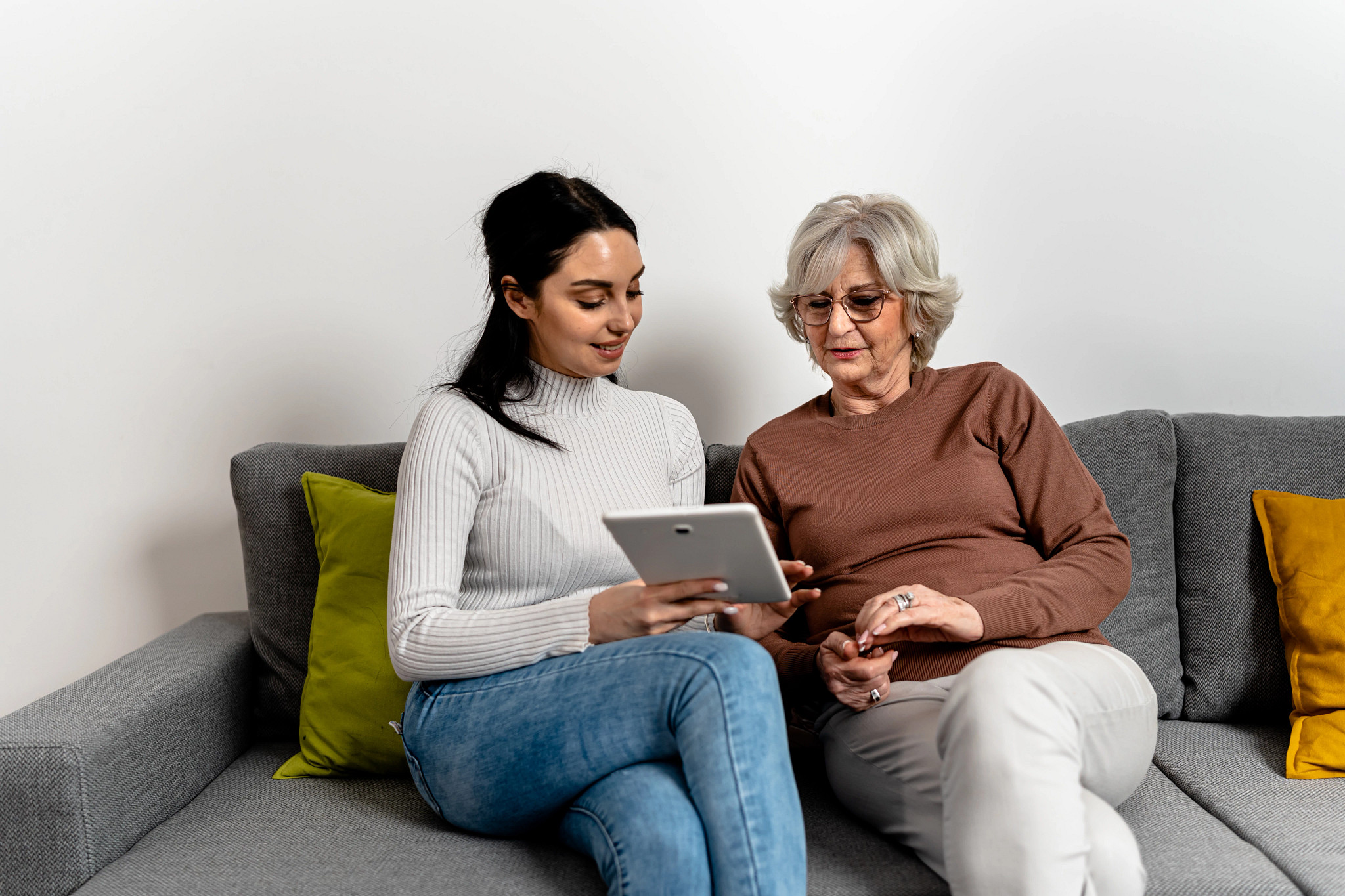 A young Caucasian woman and a senior lady having fun at home using digital tablet