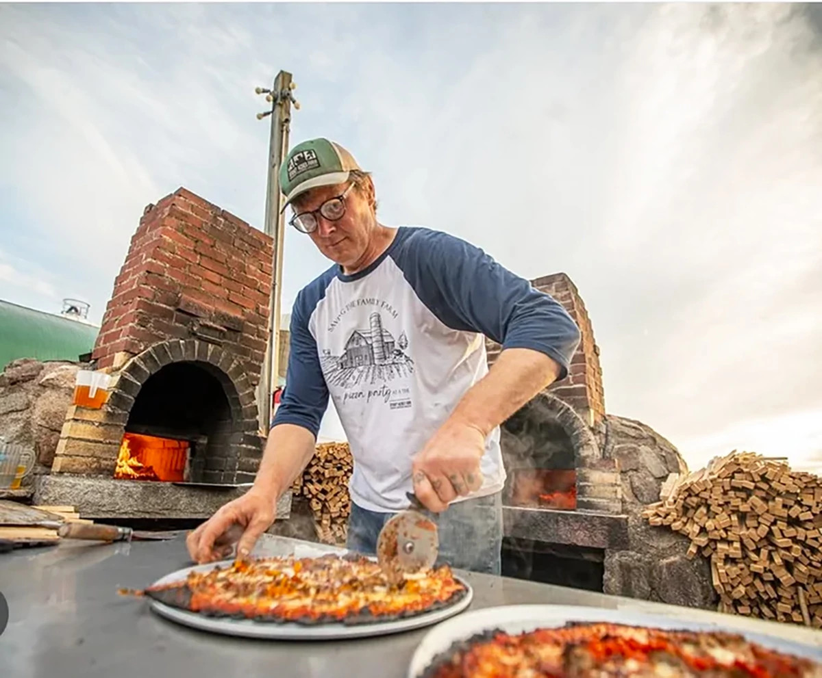 a person cutting a pizza near a fieldstone oven