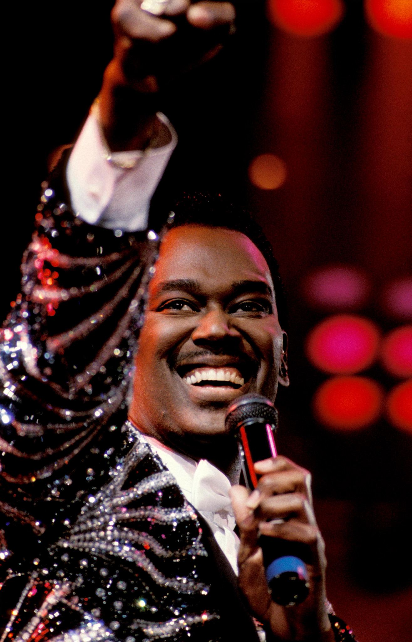 luther vandross smiling, holding a microphone, wearing a glittering jacket