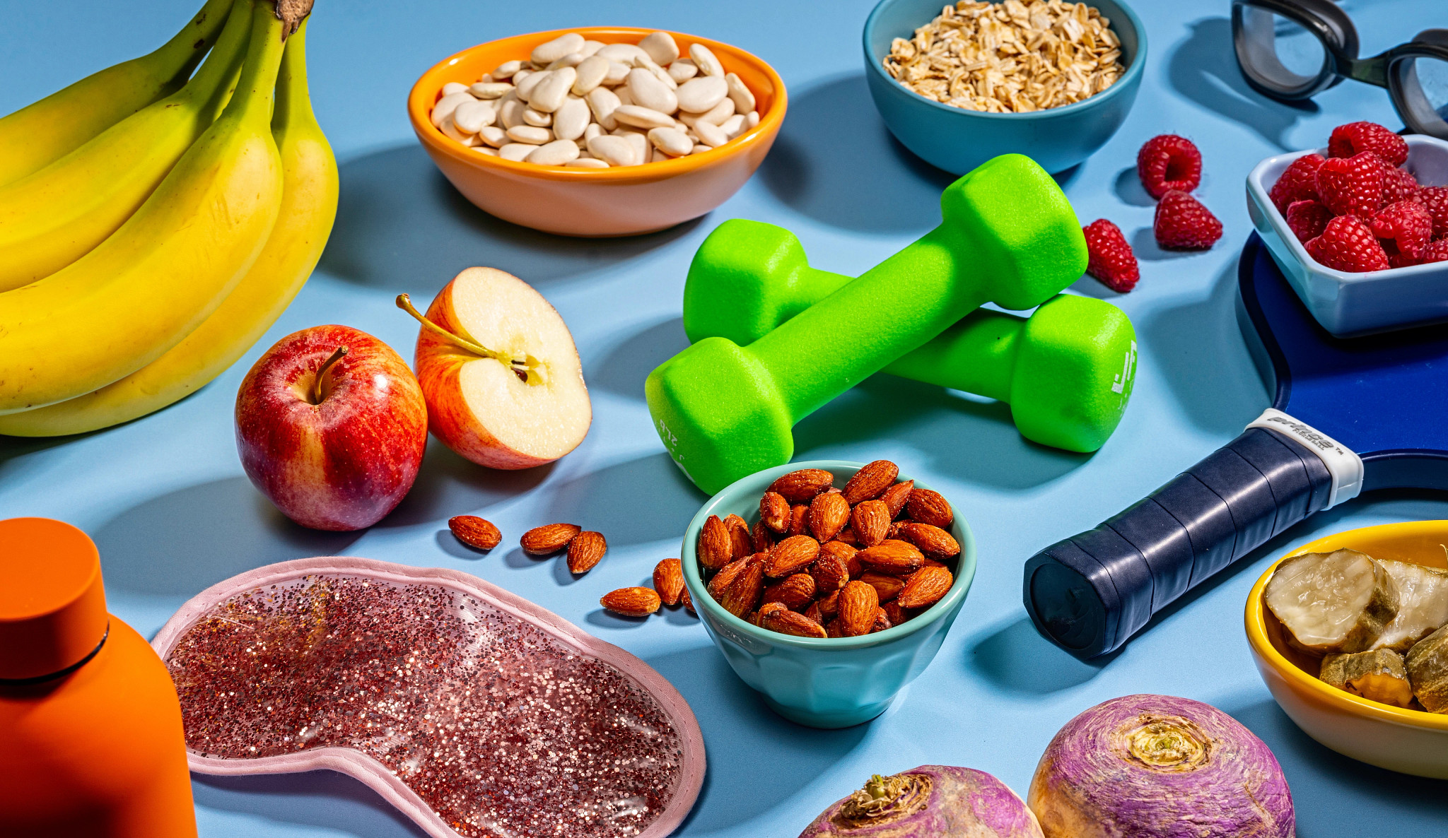Overhead view of various items like almonds, sleep mask, apples and weights on a blue background