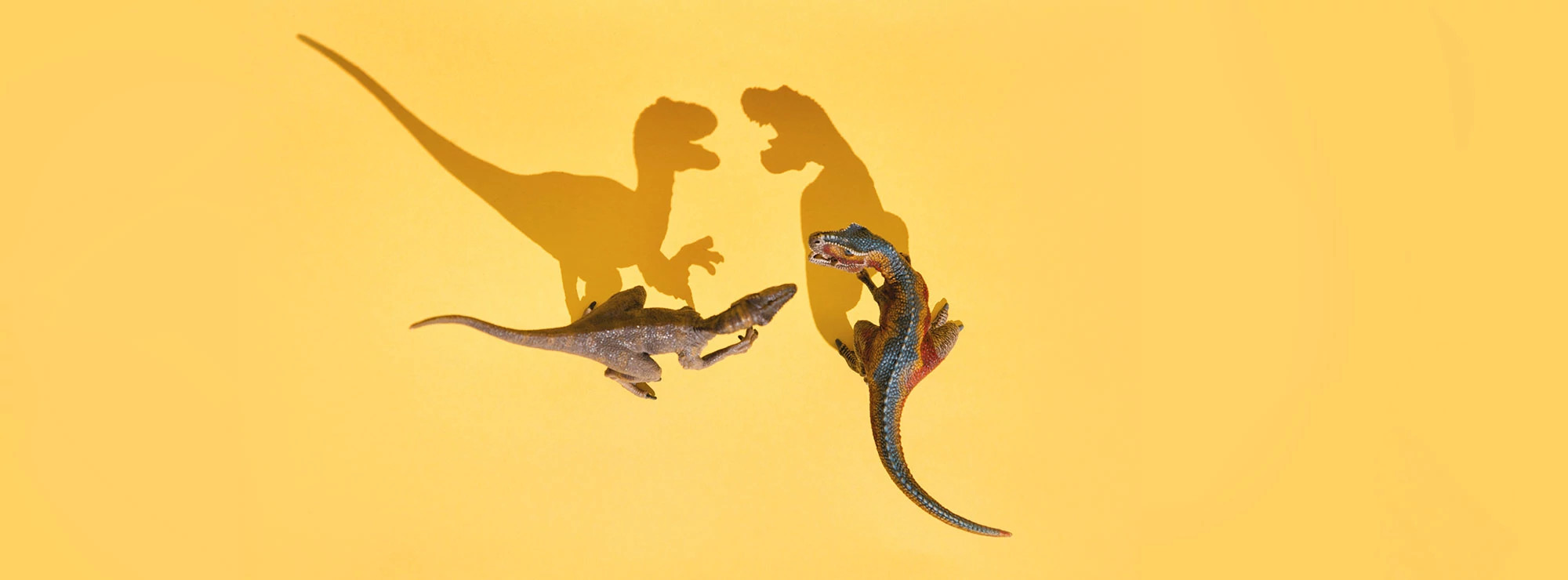 Two toy dinosaurs with mouths open casting long angry shadows