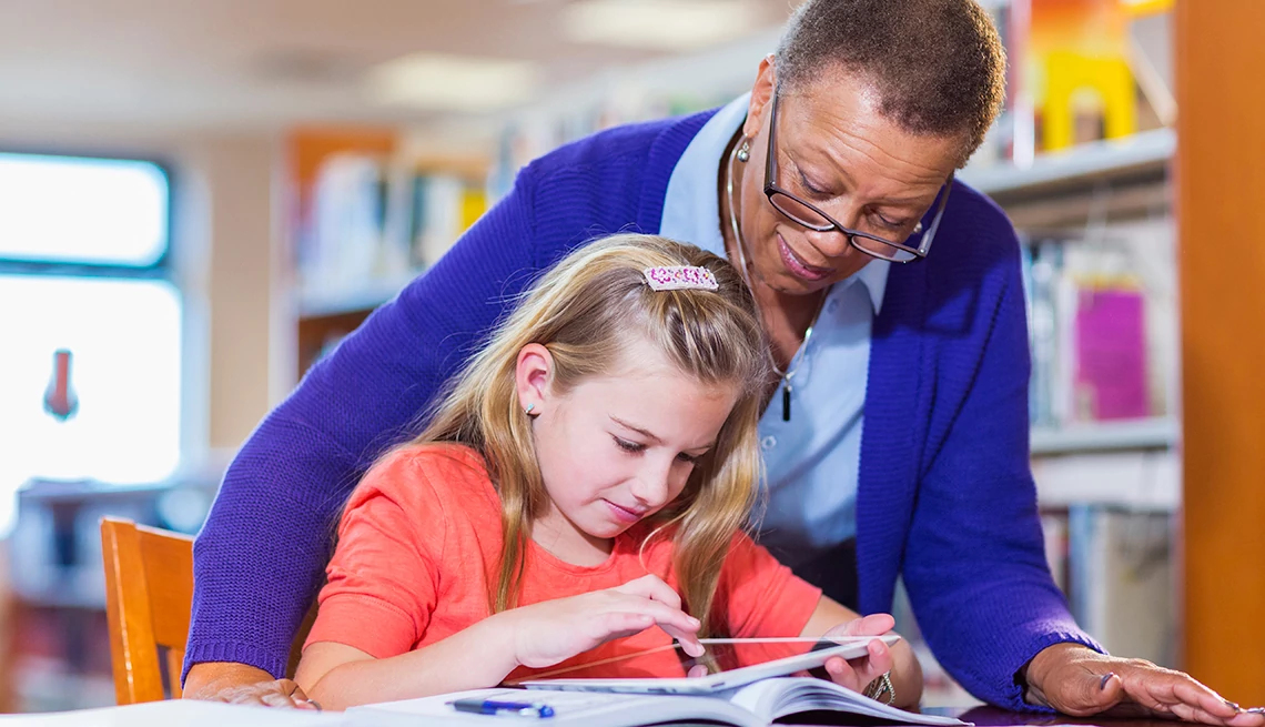 Mujer afroamericana ayudando a una niña a leer un libro en la biblioteca Mujer afroamericana ayudando a una niña a leer un libro en la biblioteca