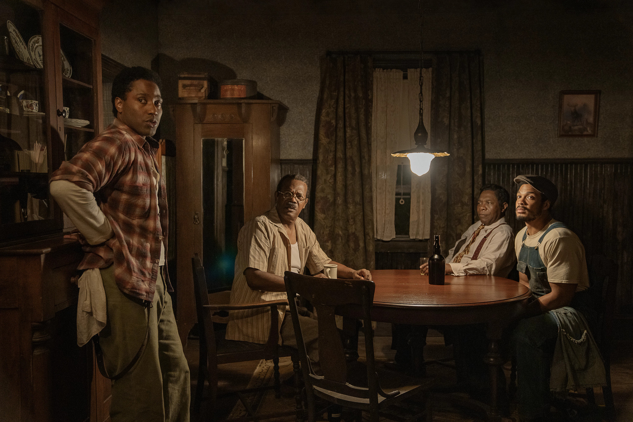John David Washington, Samuel L. Jackson, Michael Potts and Ray Fisher standing or sitting around a dining table in the Netflix film The Piano Lesson