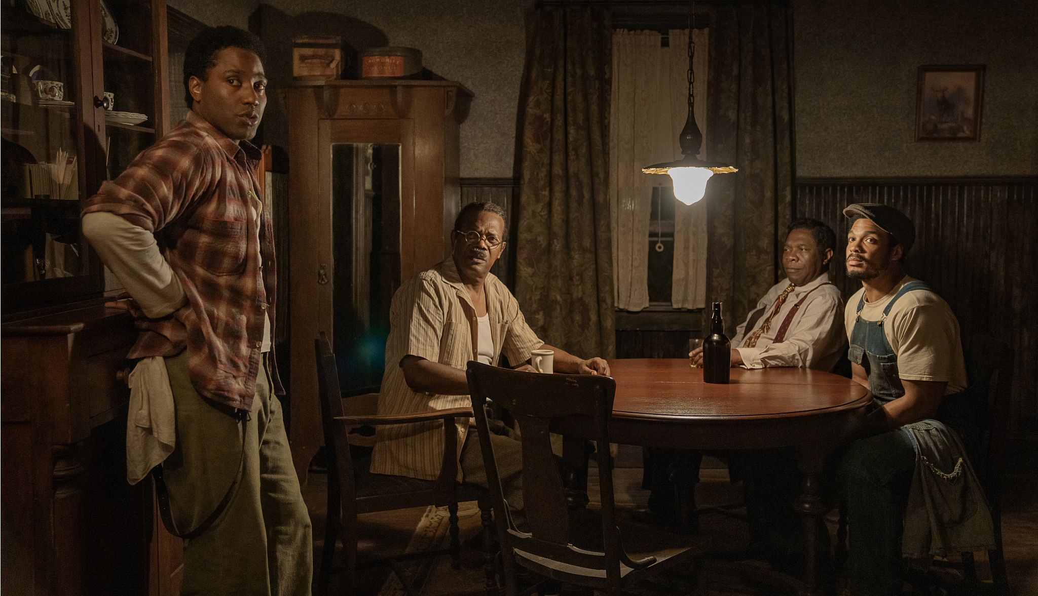 The Piano Lesson John David Washington, Samuel L. Jackson, Michael Potts and Ray Fisher standing or sitting around a dining table in the Netflix film The Piano Lesson