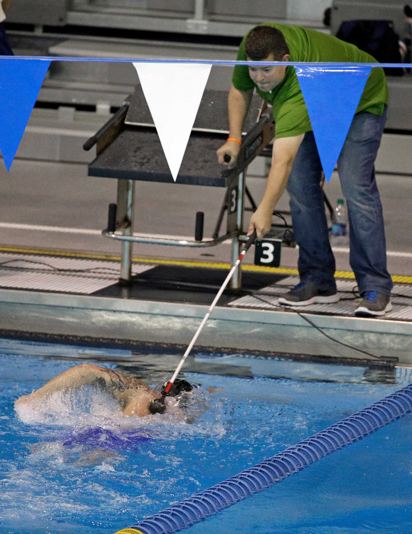 a volunteer uses a pole to tap a swimmer on the back