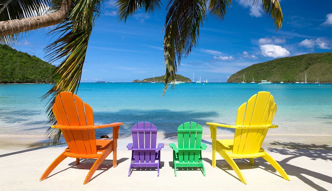 AARP Travel colorful adirondack chairs on a tropical beach with palm trees