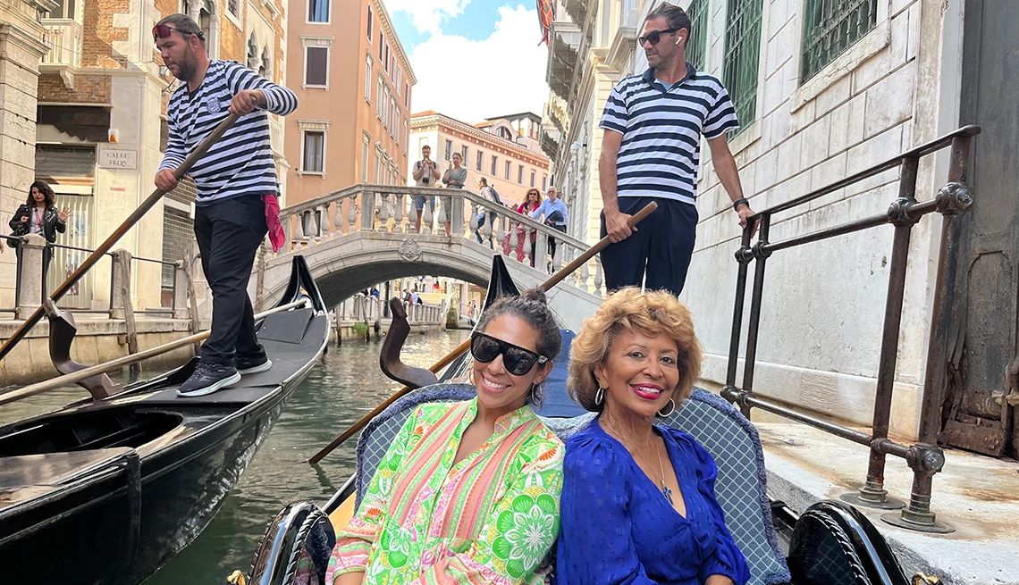 Two mature women wearing colorful outfits riding in a gondola in Venice and smiling