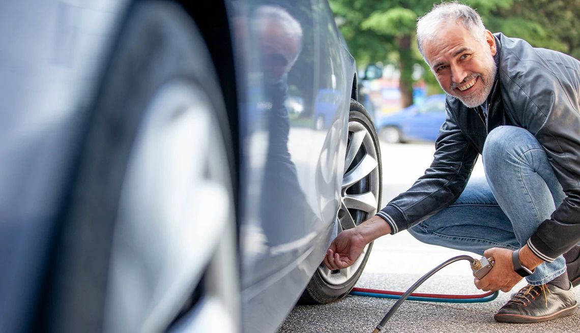 Man wearing a leather jacket and smiling put in air in his car's tires.