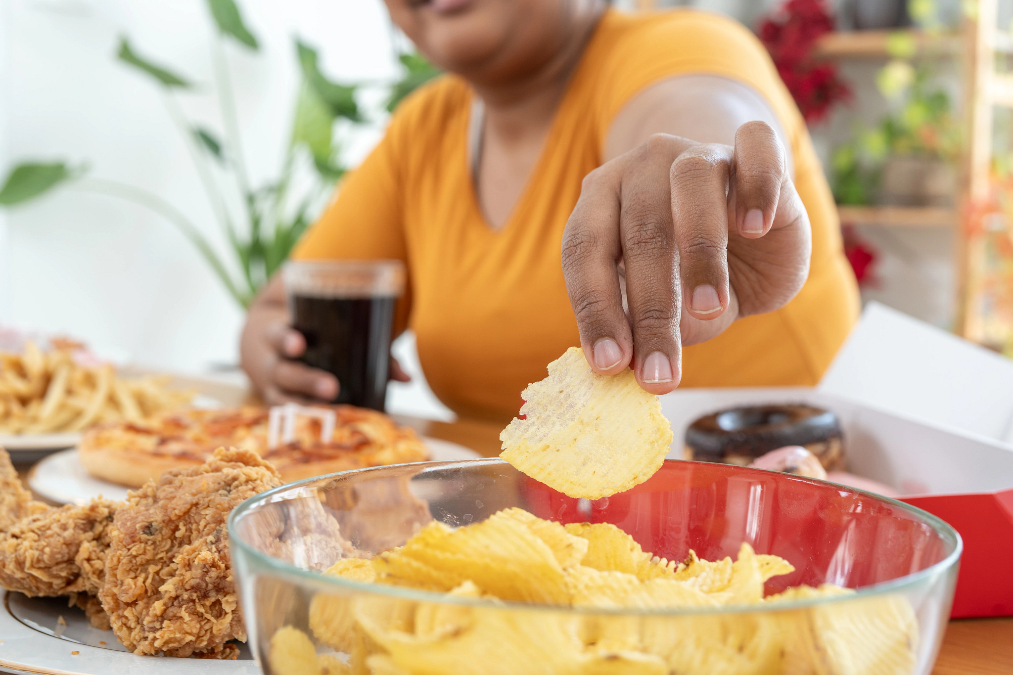 A woman reaching for a potato chip out of a bowl with a glass of soda in her other hand