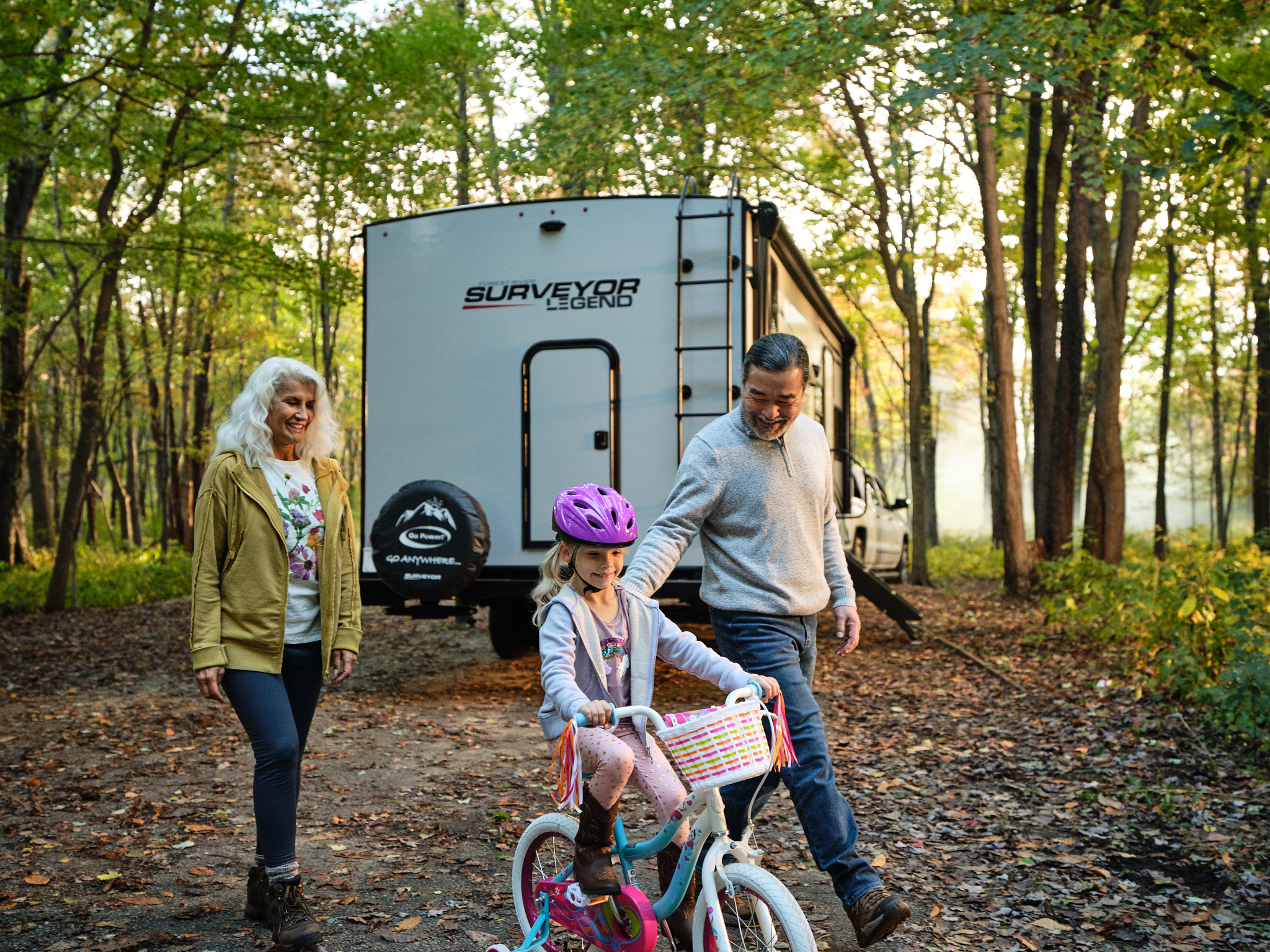 grandparents helping young daughter learn to ride a bike with a travel trailer in the background