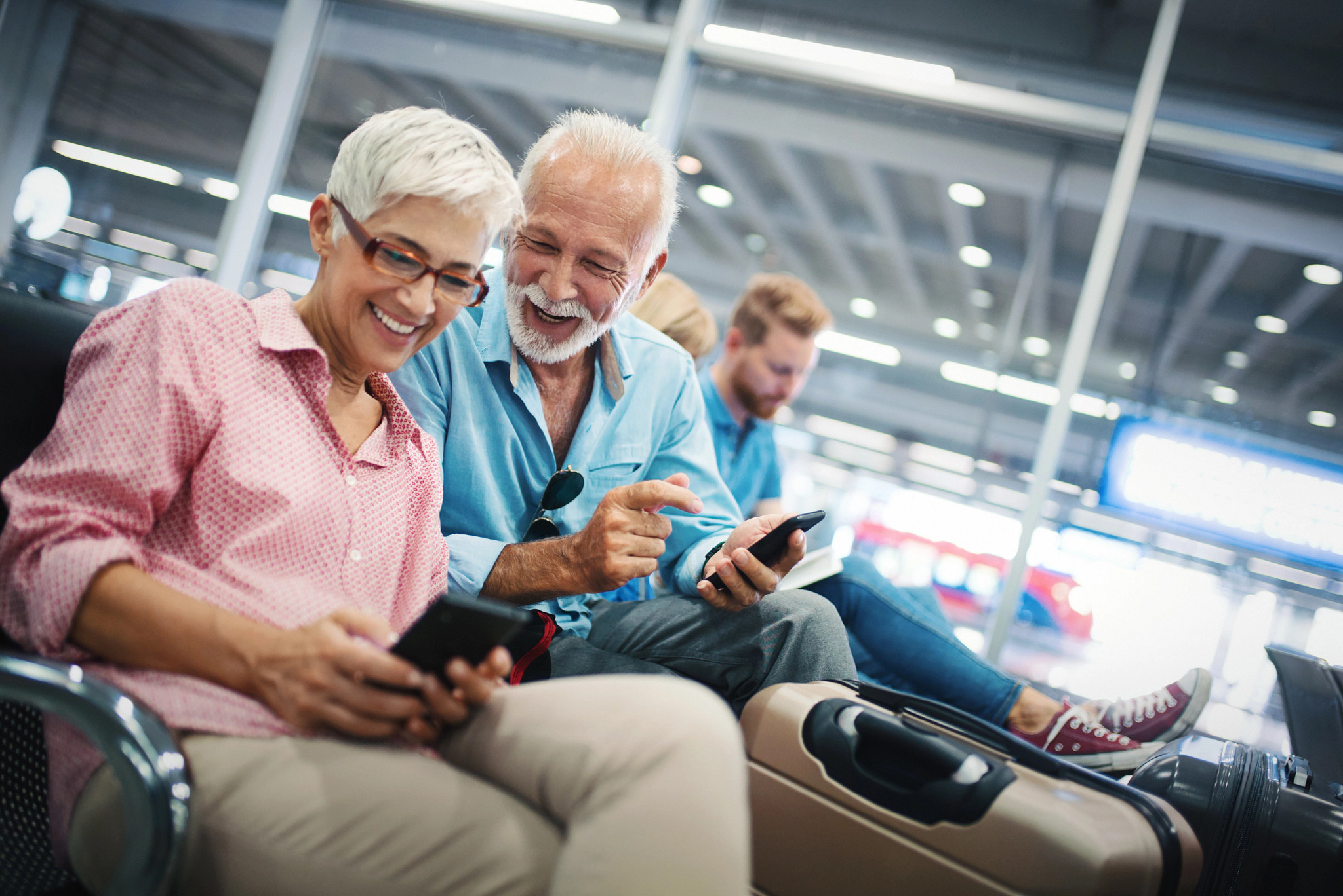 Closeup side view of a senior couple waiting for a plane at a gate. Senior couple is browsing through some social media feed and having fun.