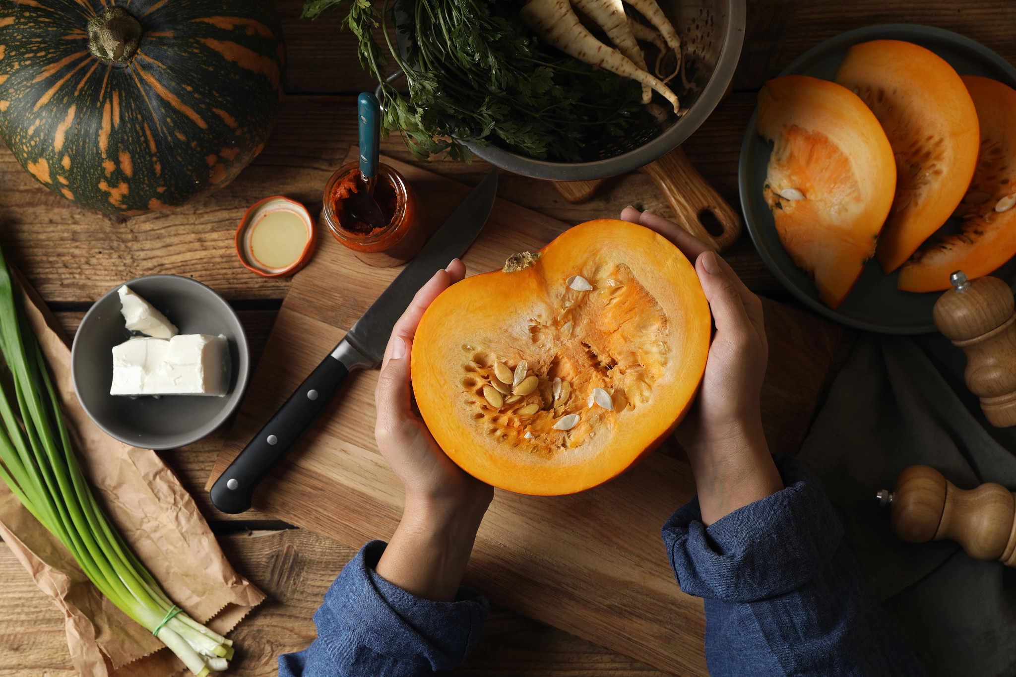 Woman with cut fresh ripe pumpkin at wooden table, top view