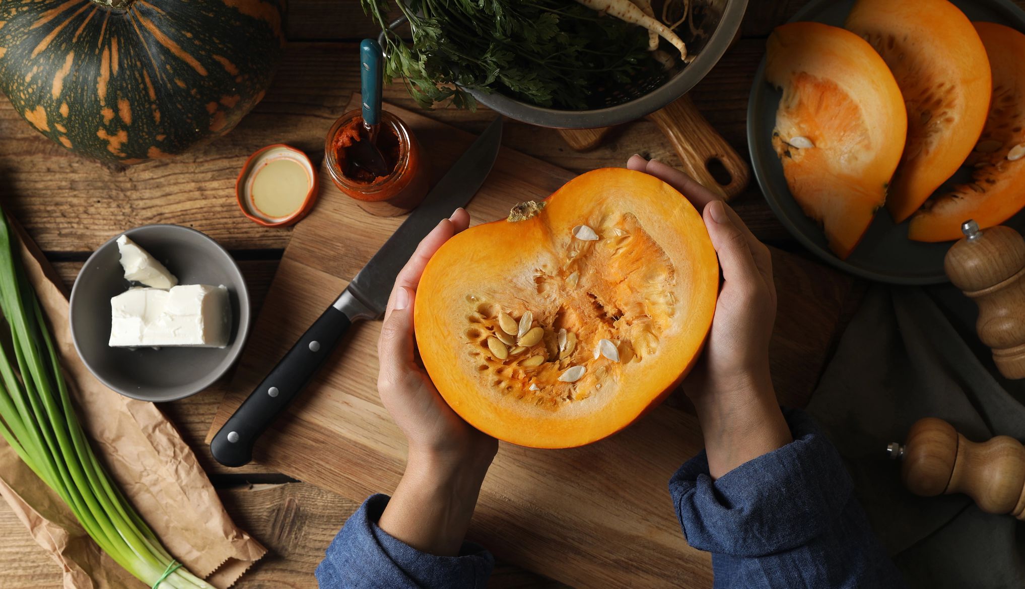 Woman with cut fresh ripe pumpkin at wooden table, top view