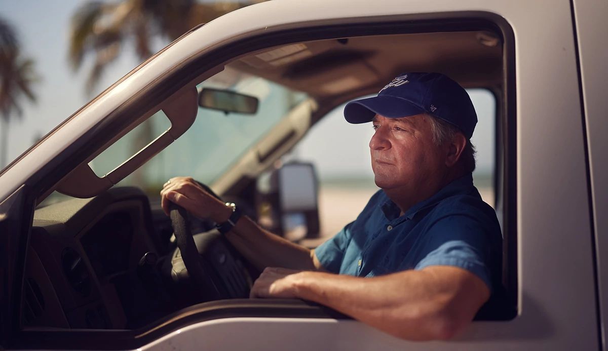 Man in a blue baseball cap in the driver’s seat of a truck