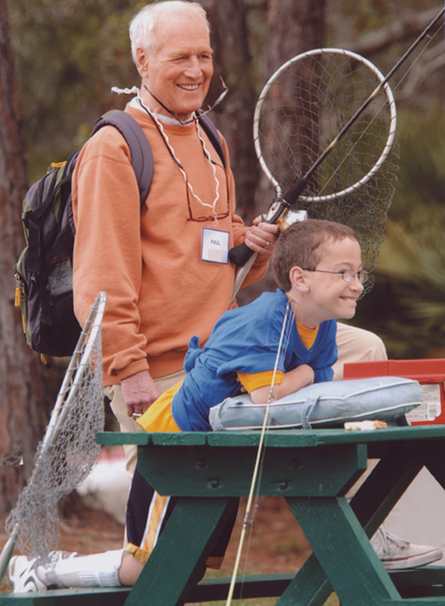 paul newman holding fishing gear, looking on as a child smiles during a summer camp activity
