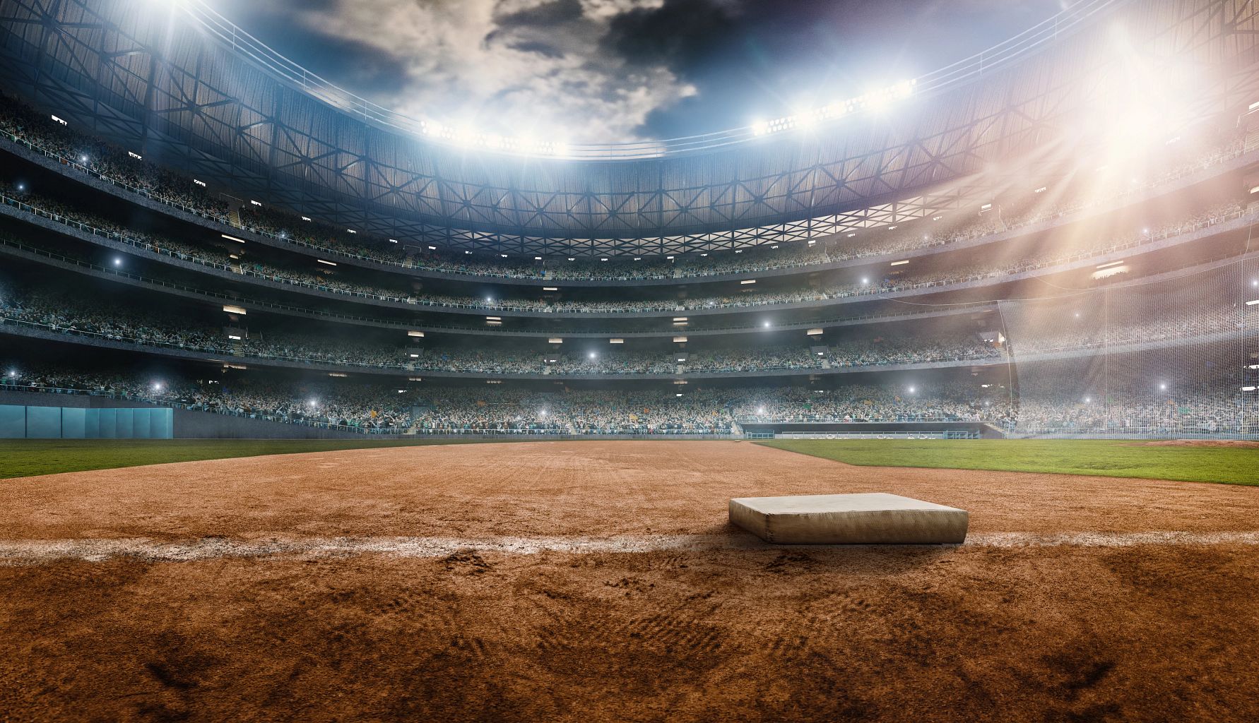 A wide angle of a outdoor baseball stadium full of spectators under a stormy night sky. A wide angle of a outdoor baseball stadium full of spectators under a stormy night sky.