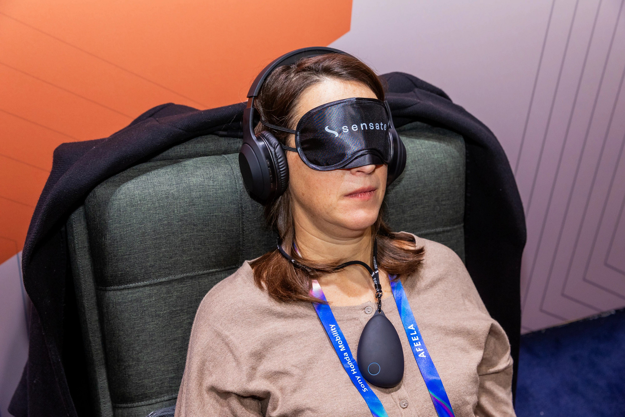 a woman sitting in a chair while wearing headphones, an eyecover and a device around her neck
