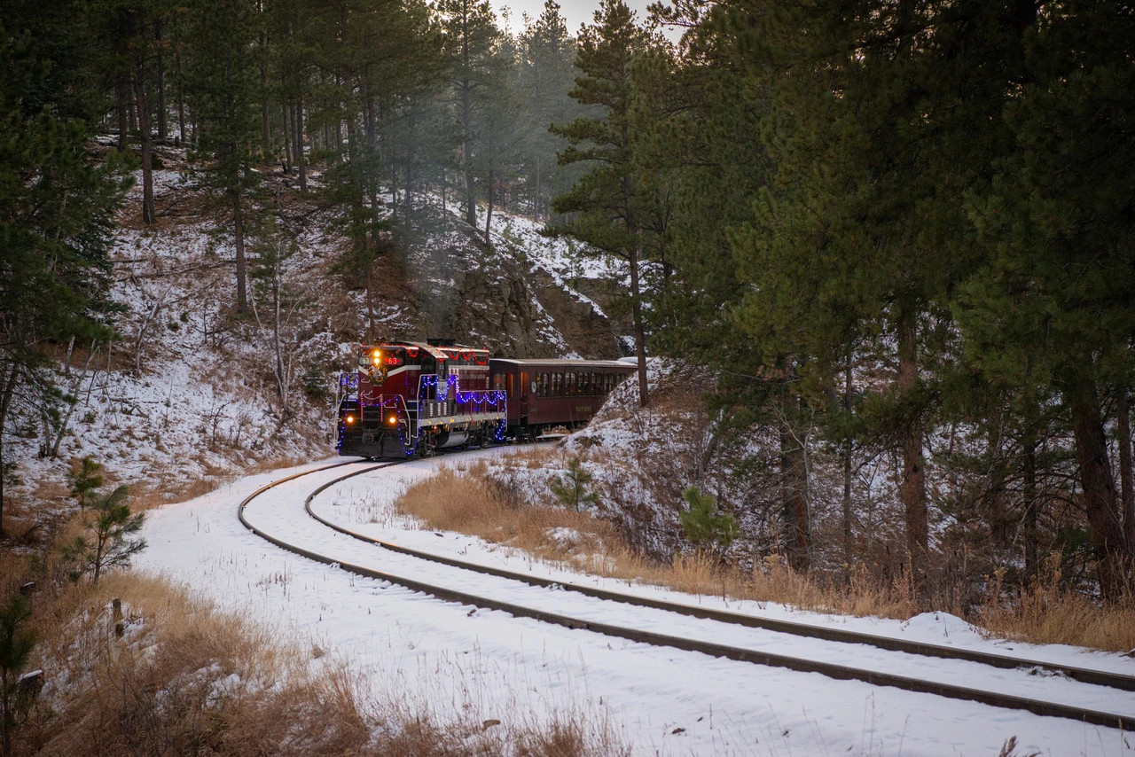 a train with holiday lights travels along a snow covered track