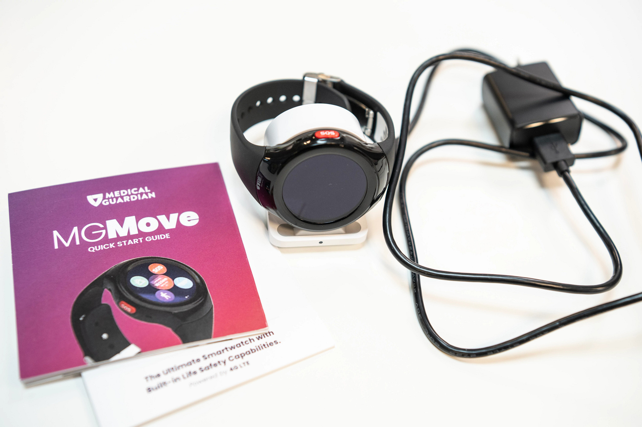 The Medical Guardian MGMove next to a charger and a product pamphlet