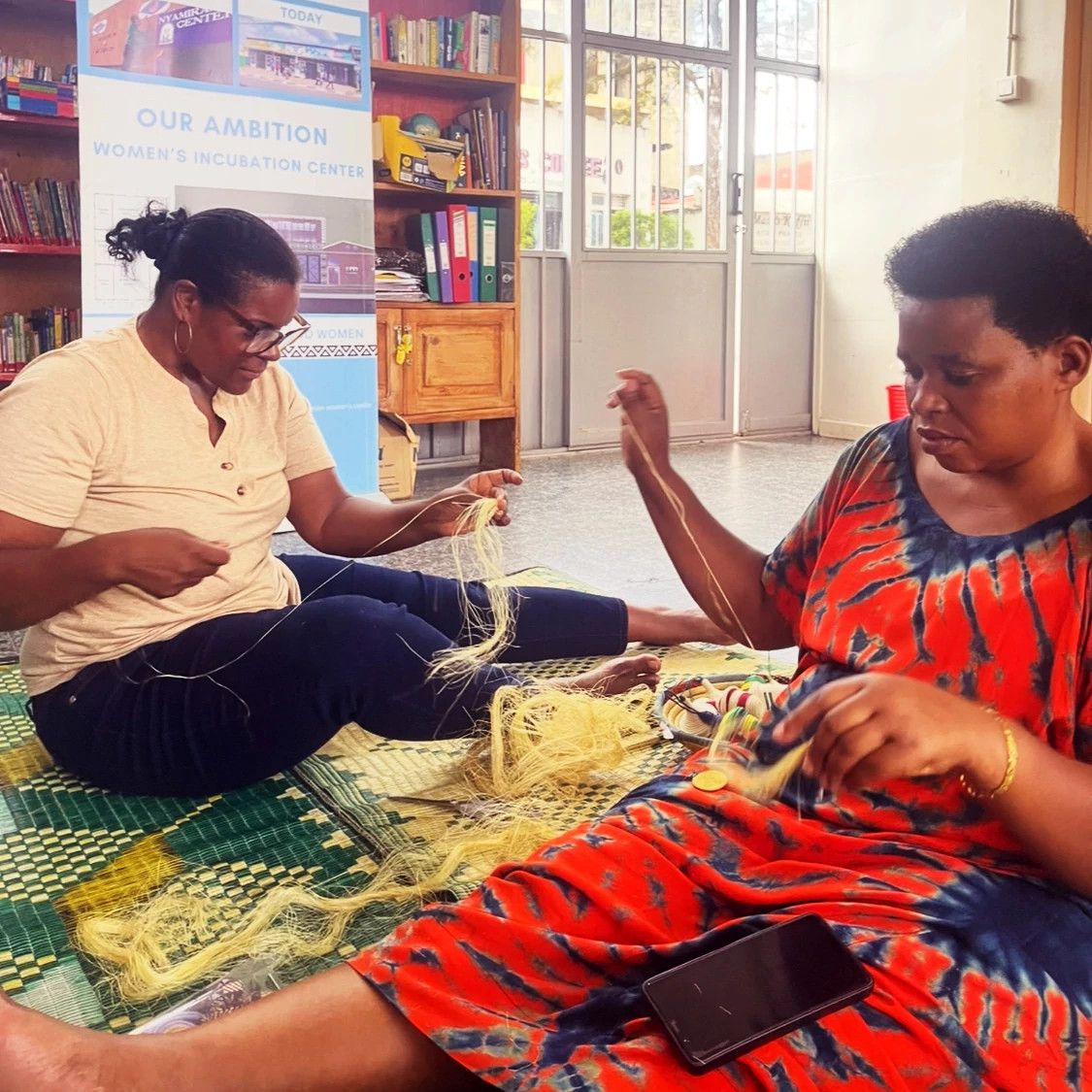 two women sitting on a rug and weaving