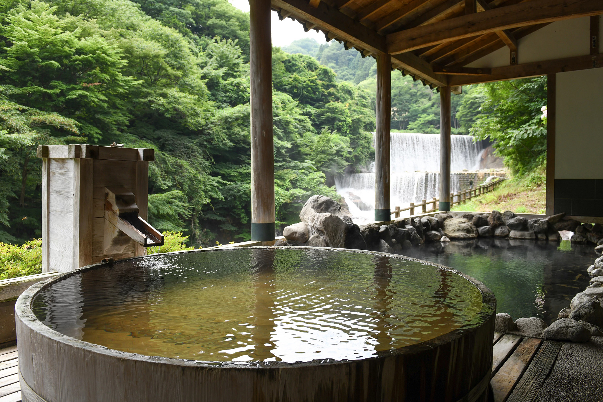 an outdoor bathhouse with a waterfall in the background in japan