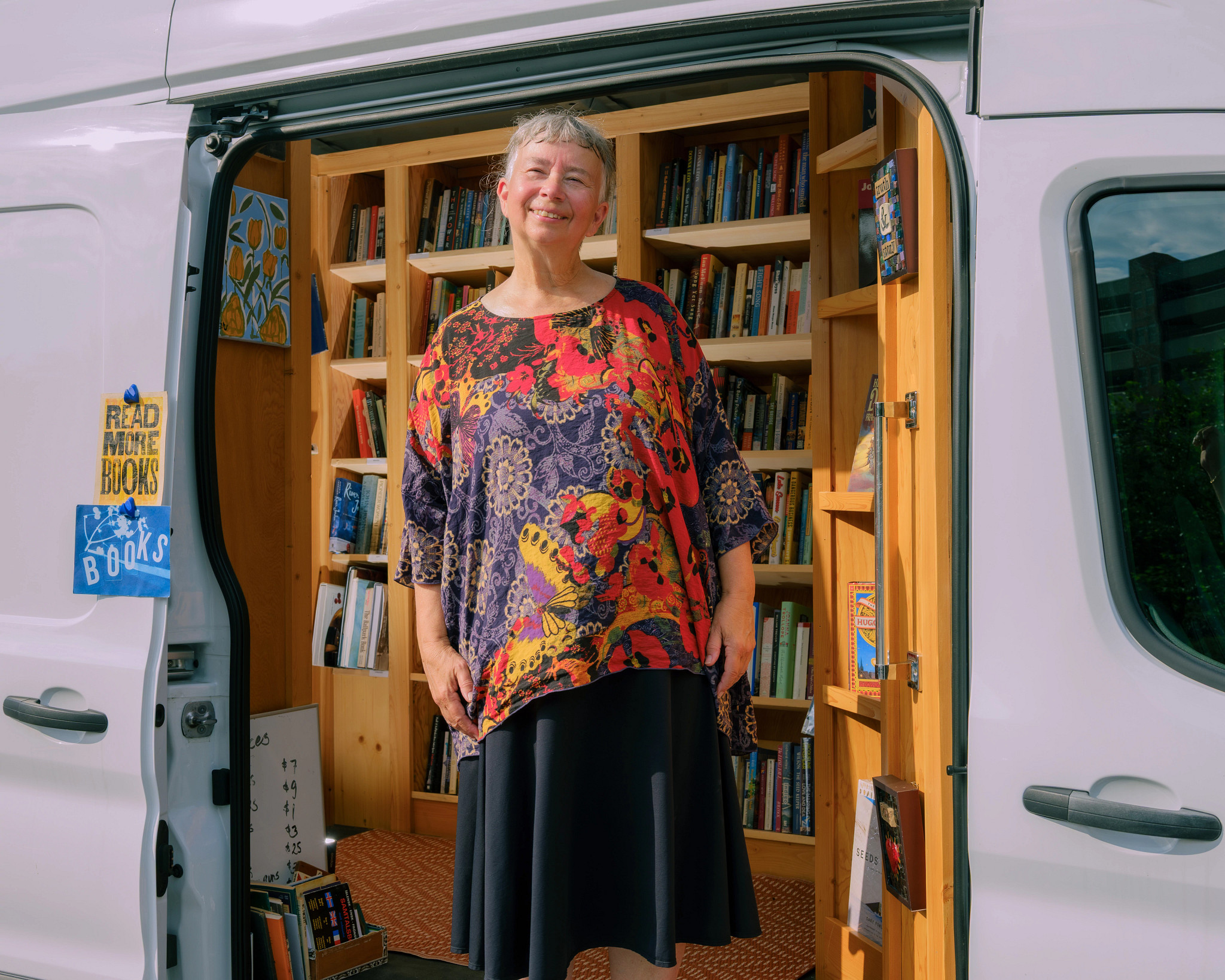 A photo shows Rita Collins standing inside the van that houses her traveling bookstore