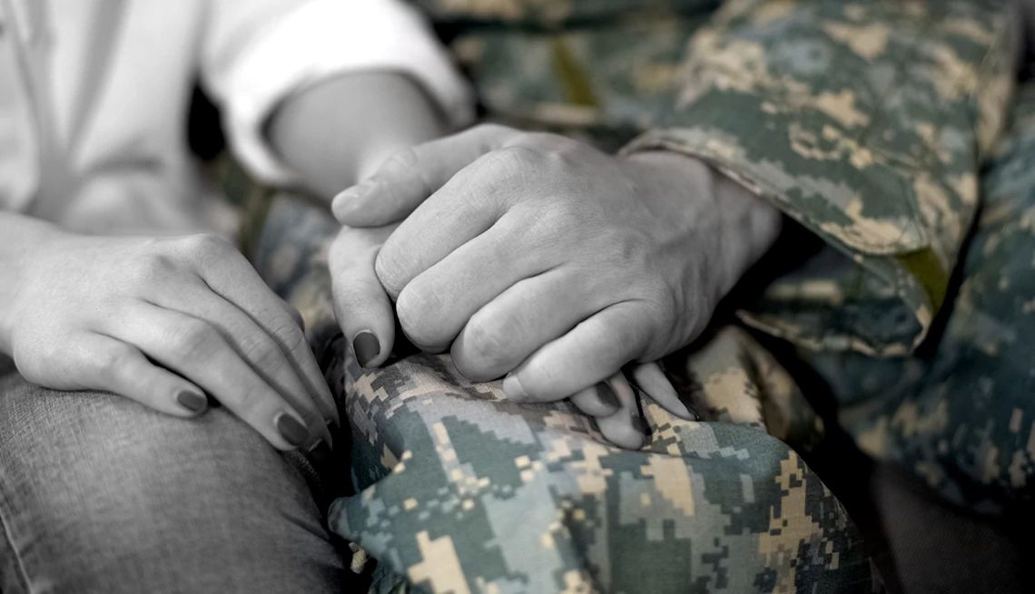 Las manos entrelazadas de una mujer y un hombre vestido en uniforme militar.