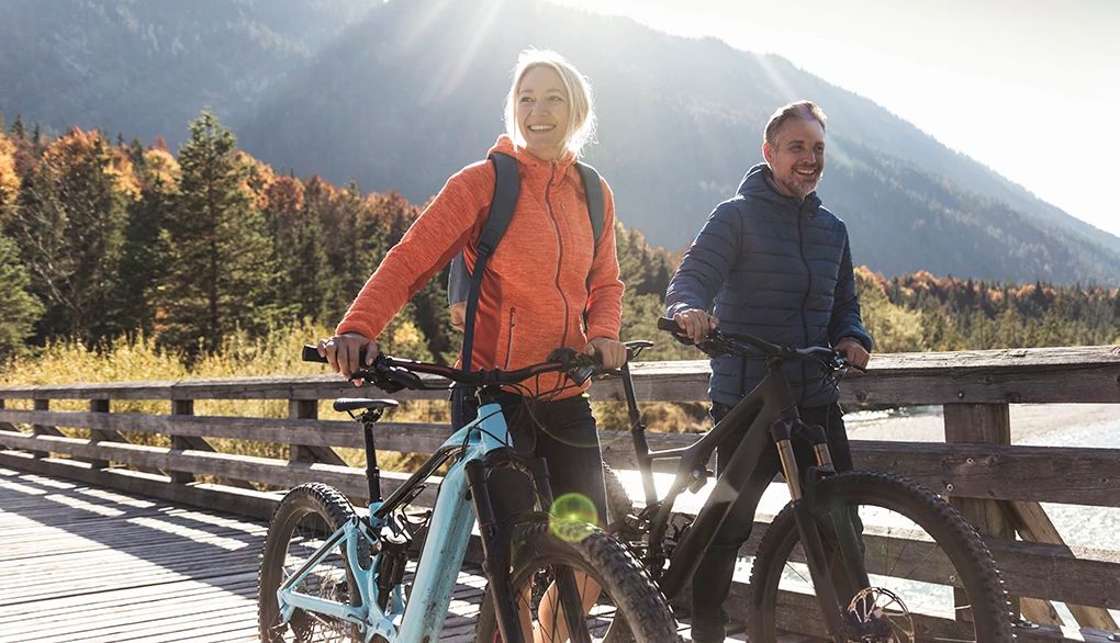 Exercise in your 40s may be beneficial for your brain health later in life A man and woman walking across a bridge with their bikes in the mountains