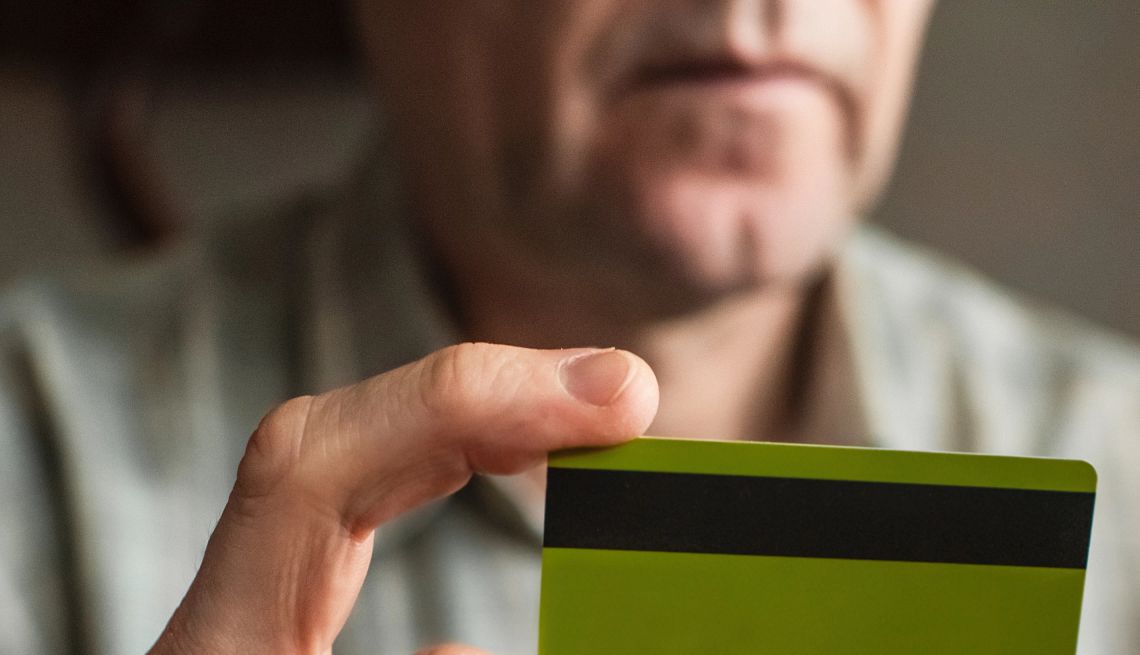 Un hombre mayor sostiene una tarjeta de crédito y un teléfono