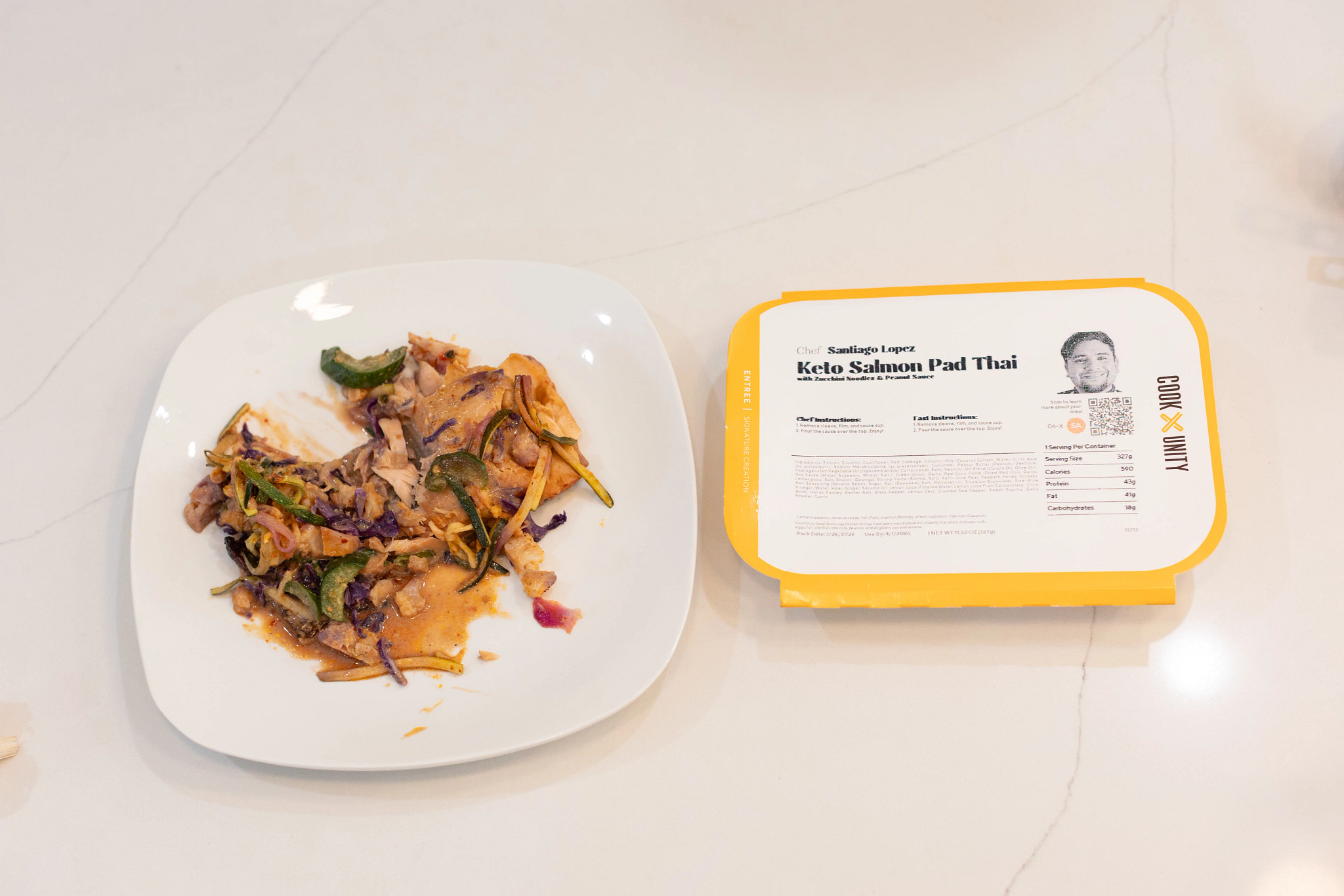 A prepared CookUnity meal on a white plate next to its packaging
