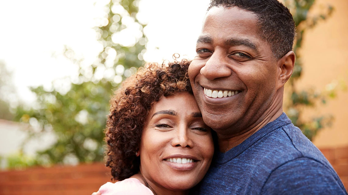 Happy middle aged black couple embracing smile to camera, close up