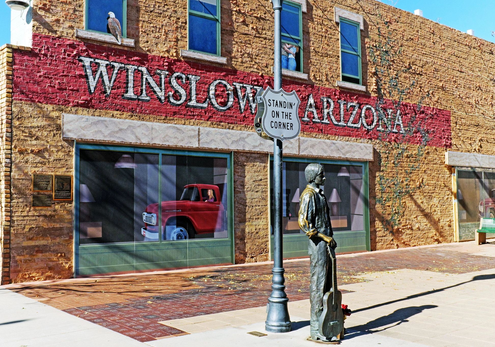 Standing on the Corner Park a statue next to a sign that reads "Standing on the Corner" in front of a brick wall