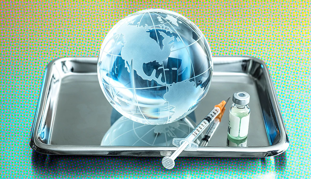 A glass globe, syringe, and vaccine vial resting on a silver medical tray.