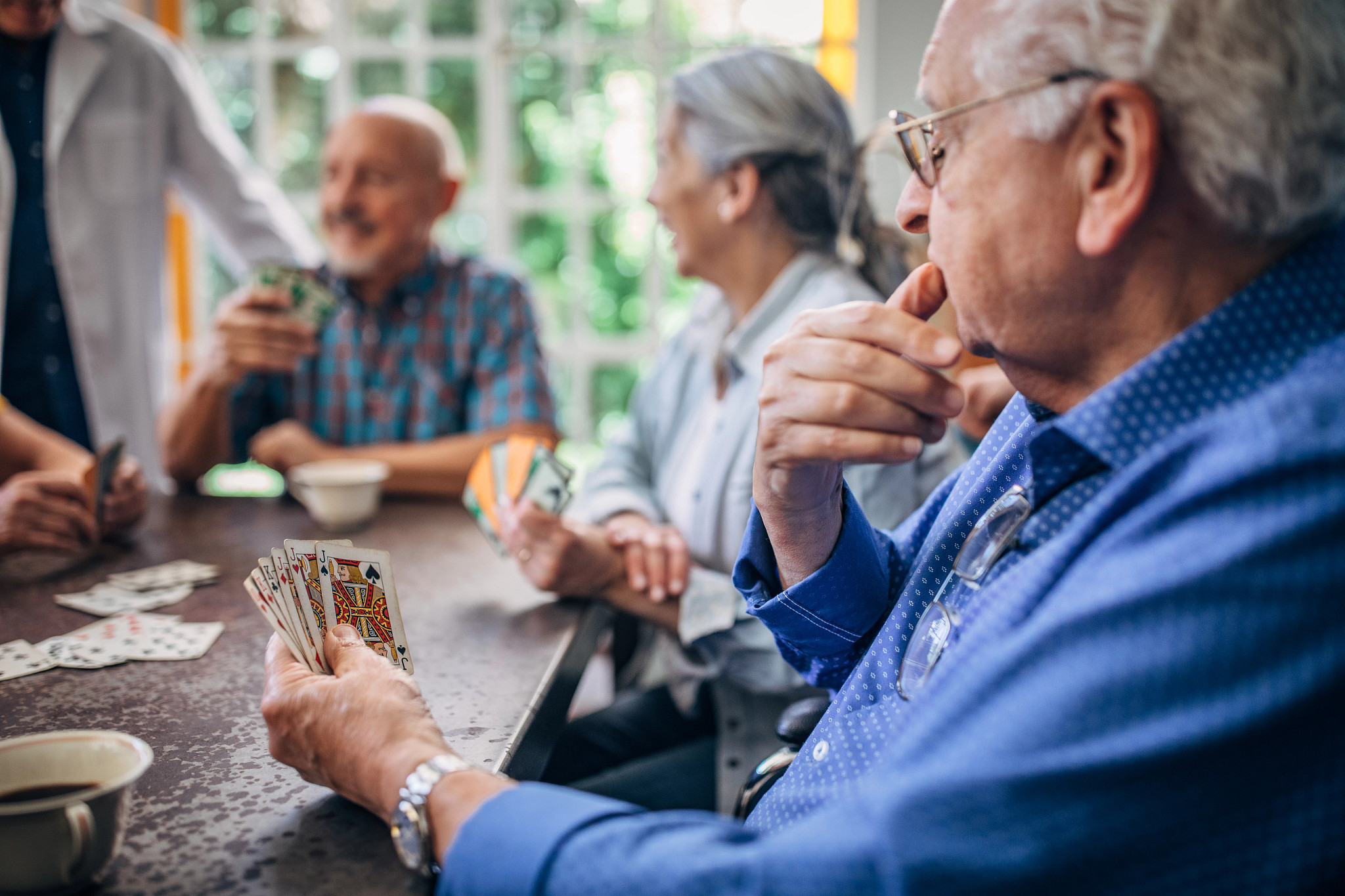 Group of people, senior man playing cards with friends in nursing home.