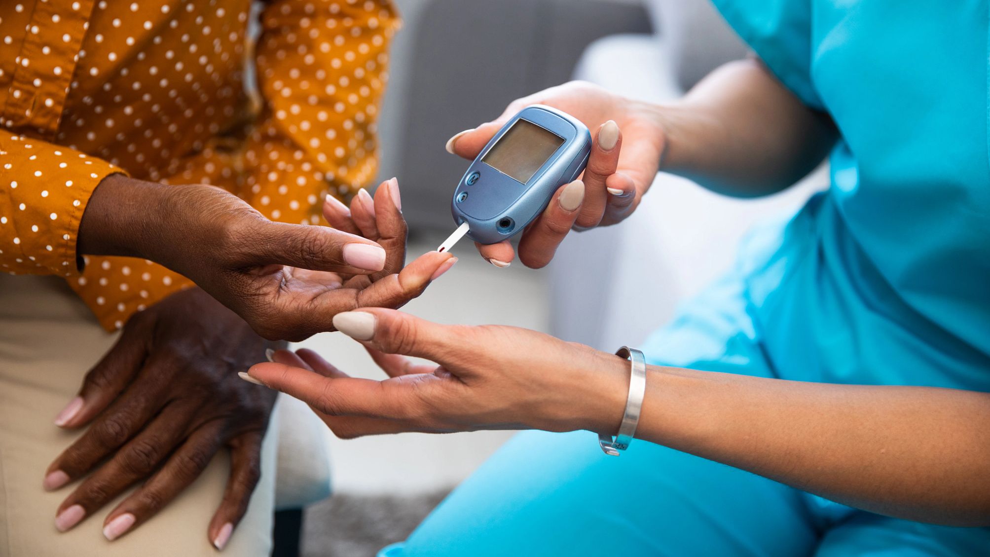 How to Care for Someone With Diabetes a caregiver gets blood from a patient's finger to test with a glucose monitor