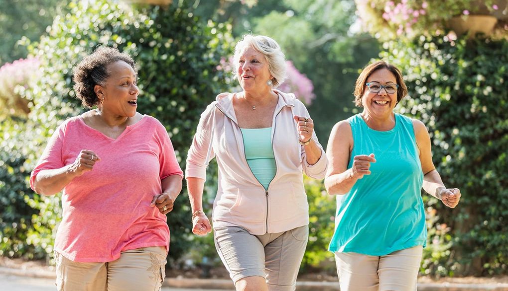 Find a friend to commit to doing regular exercise Three women smiling and power walking together outside