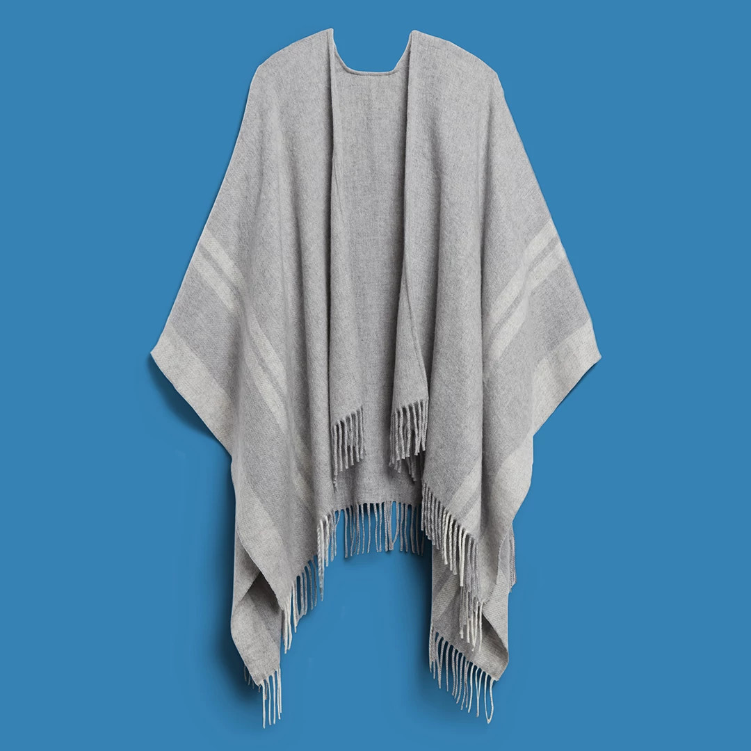 Light gray fringed poncho wrap displayed against a blue background