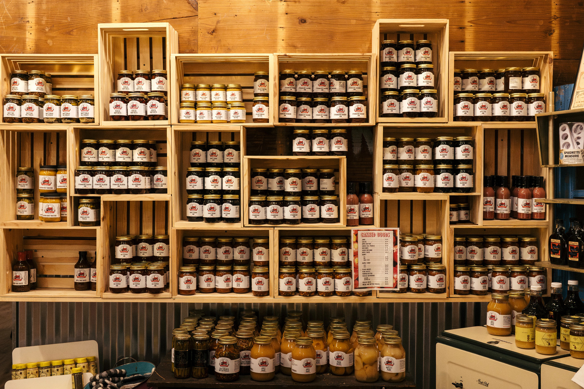 Wooden shelves stacked with glass jars of homemade jams, sauces, and preserved foods arranged in a rustic pantry setting