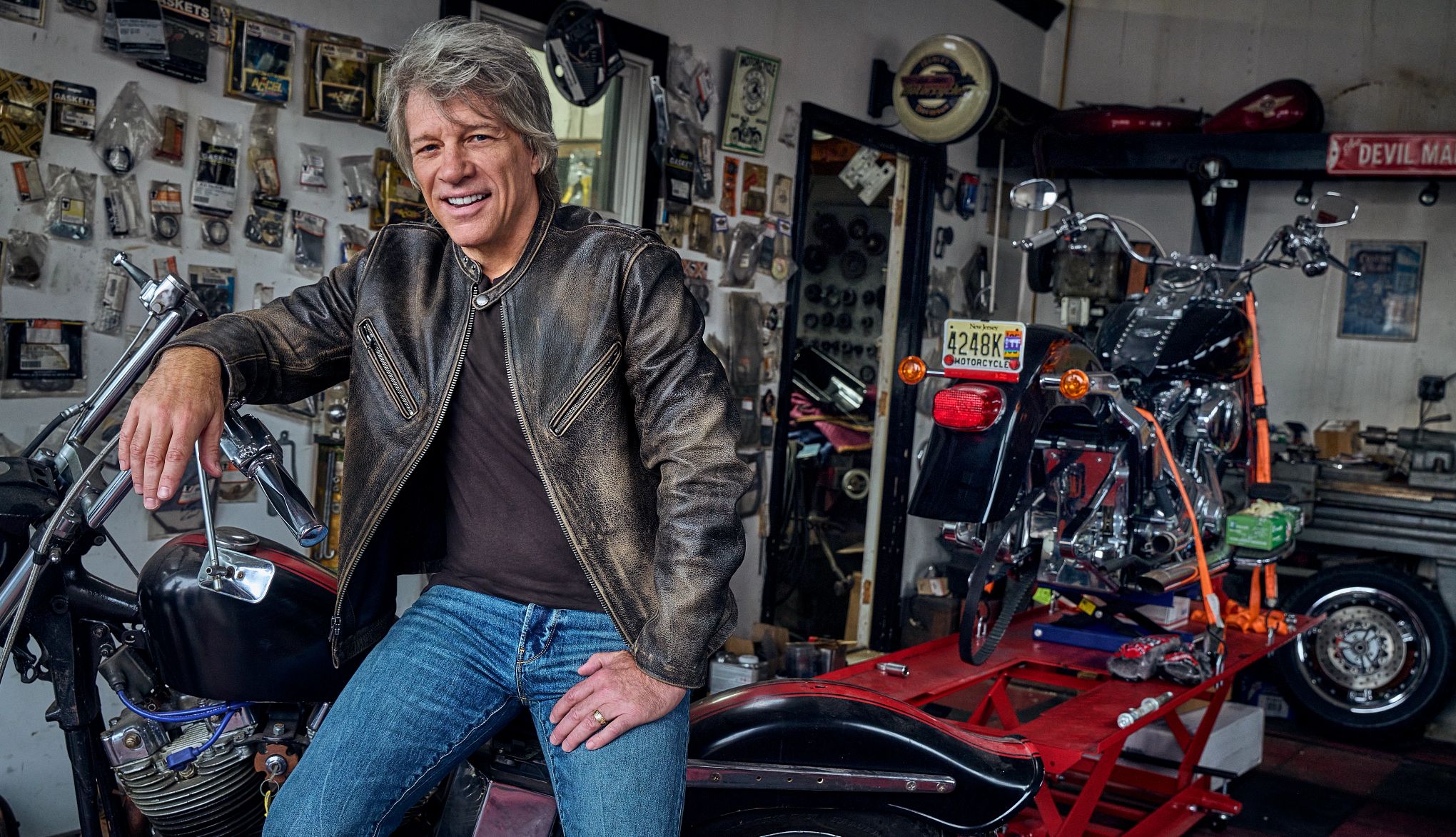 Jon Bon Jovi sitting on a motorcycle in a garage