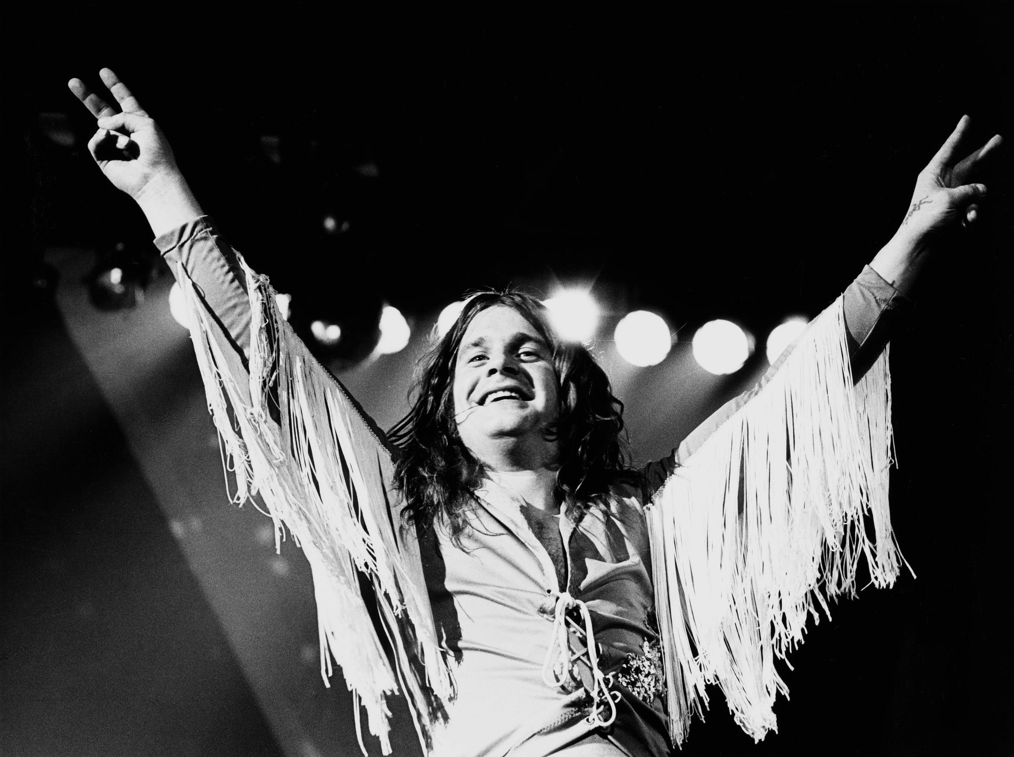 Ozzy Osbourne giving a double peace sign and smiling broadly