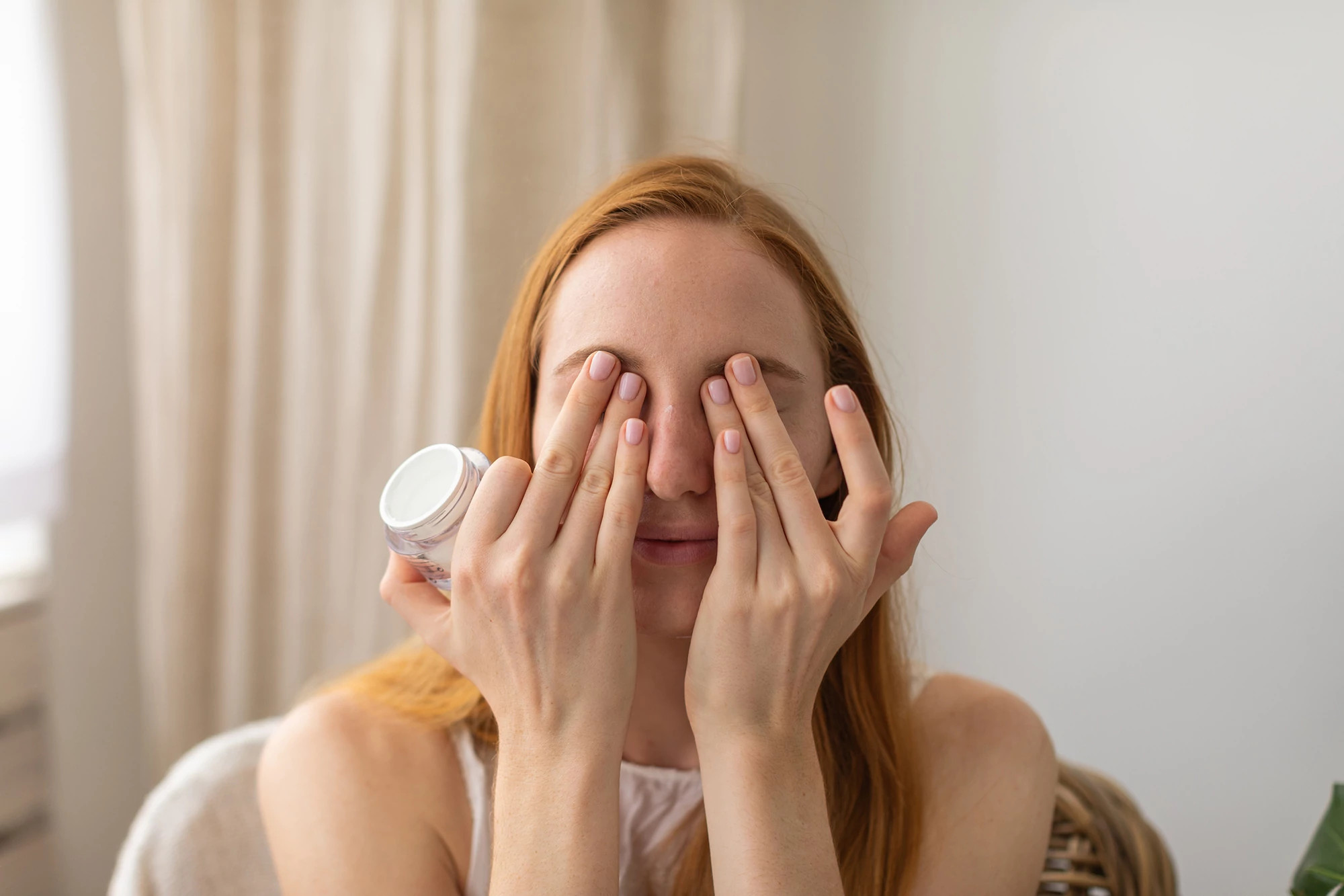 woman putting eye cream over her eyes at home