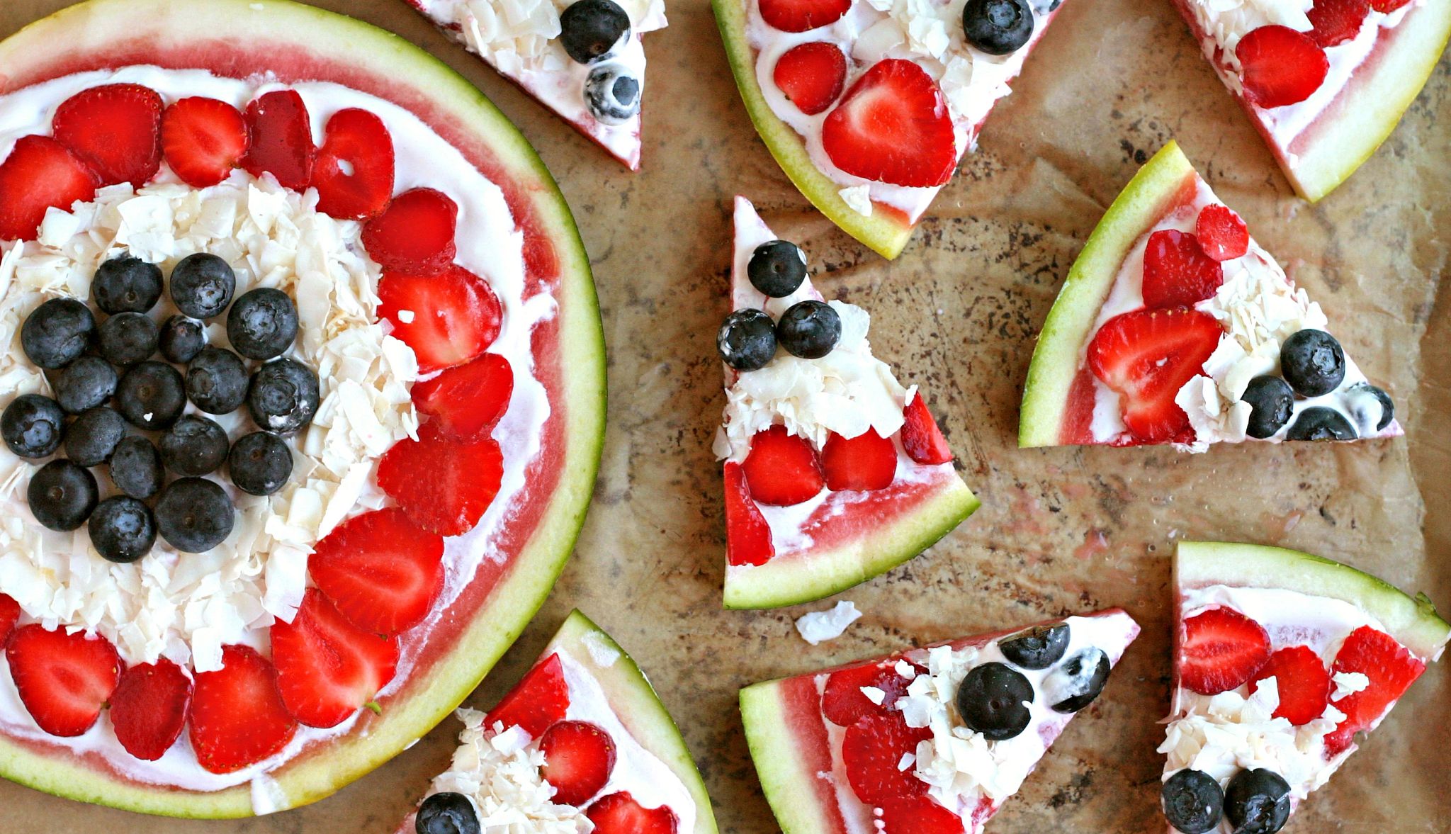 Watermelon Pizza A watermelon pizza is pictured, featuring blueberries, strawberries and nondairy yogurt toppings. The whole pie is on the left, with slices on the right side.